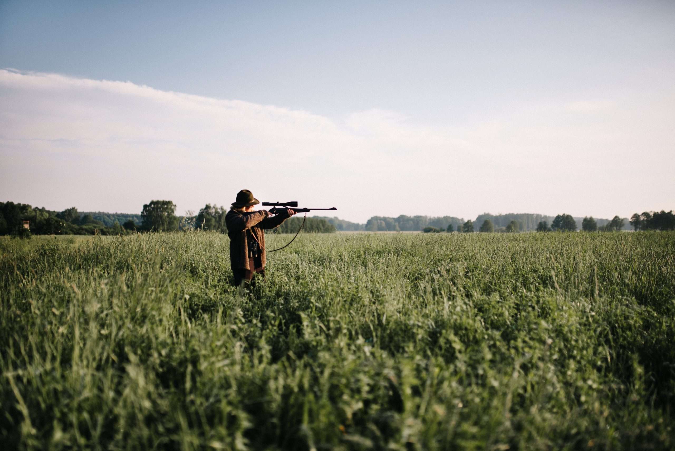 person aiming with gun amidst grass field